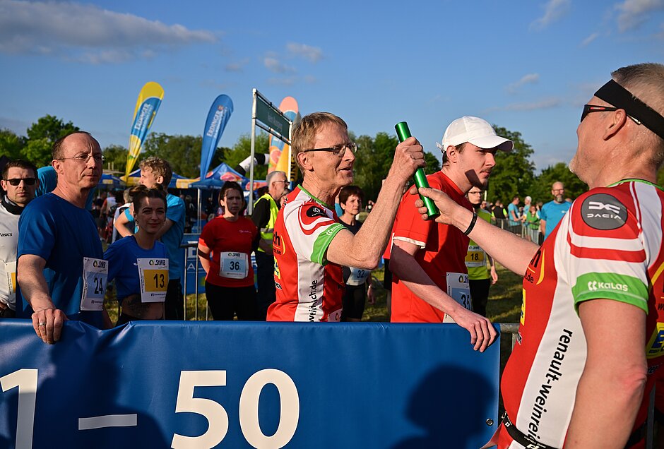 Team Staffel Brandenburg: Männlicher Läufer übergibt Staffelstab an Teamkollegen, weitere Teilnehmer warten in der Wechselzone @ SCC EVENTS / Petko Beier