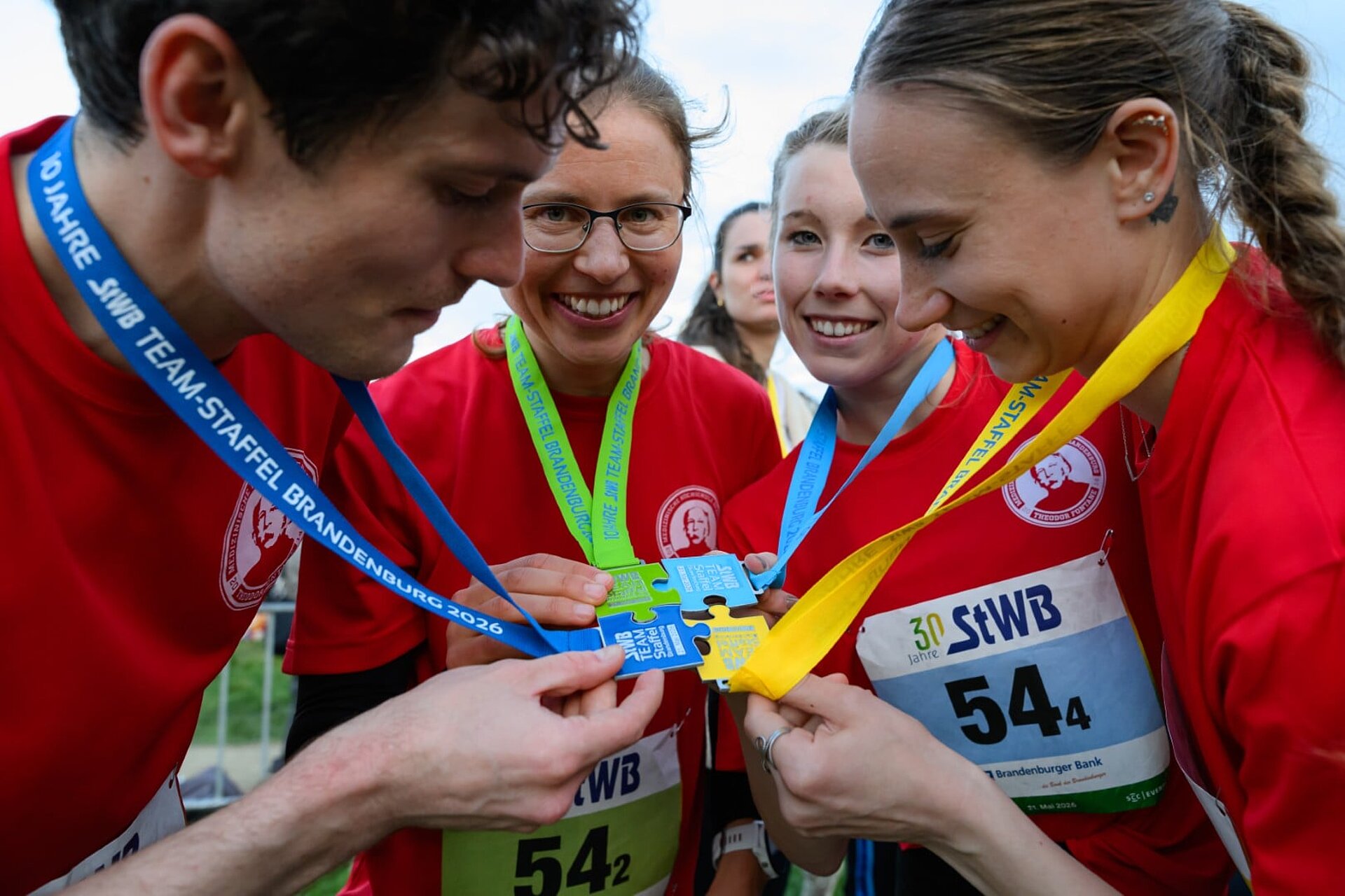 Vier glückliche Teilnehmende setzen ihre Einzelmedaillen, jeweils in Form eines Puzzleteils, zur Teammedaille zusammen.