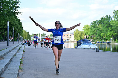 Team Staffel Brandenburg Fotos (2023): Läuferin im blauen T-Shirt recht die Arme in die Luft und steuert freudestrahlend auf die Kamera zu