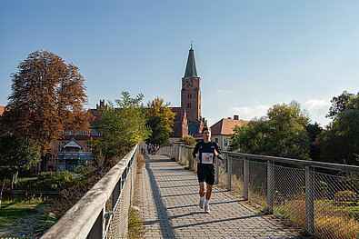 Team Staffel Brandenburg Fotos (2021): Läufer überquert eine Brücke, im Hintergrund der Dom zu Brandenburg